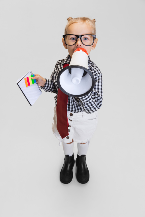 Little girl with glasses in casual clothing shouting in megaphone