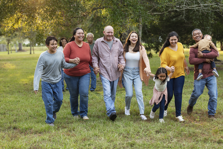 Multiracial extended family run playfully holding hands